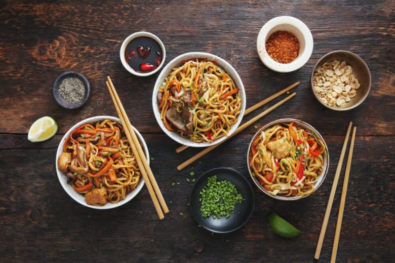 Bowls of Asian food with chicken, beef and vegetables chow mein and rice with pork.