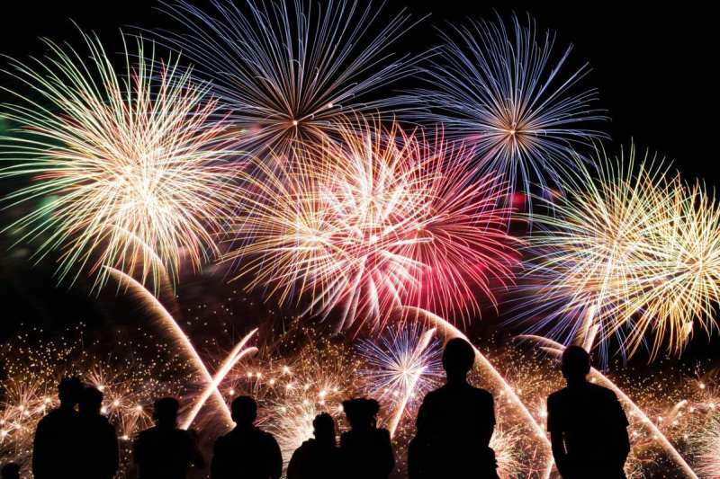 Silhouettes of people watching fireworks at night.