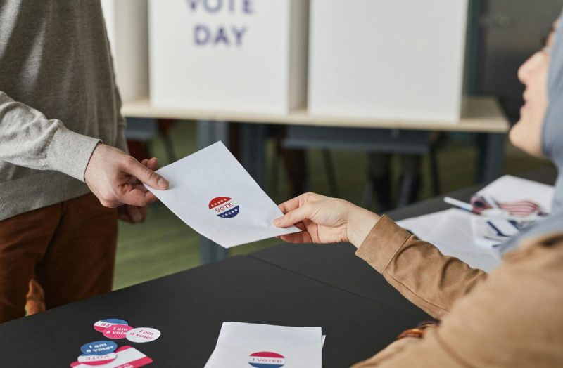 Person handing over paper with "Vote" sticker on it.