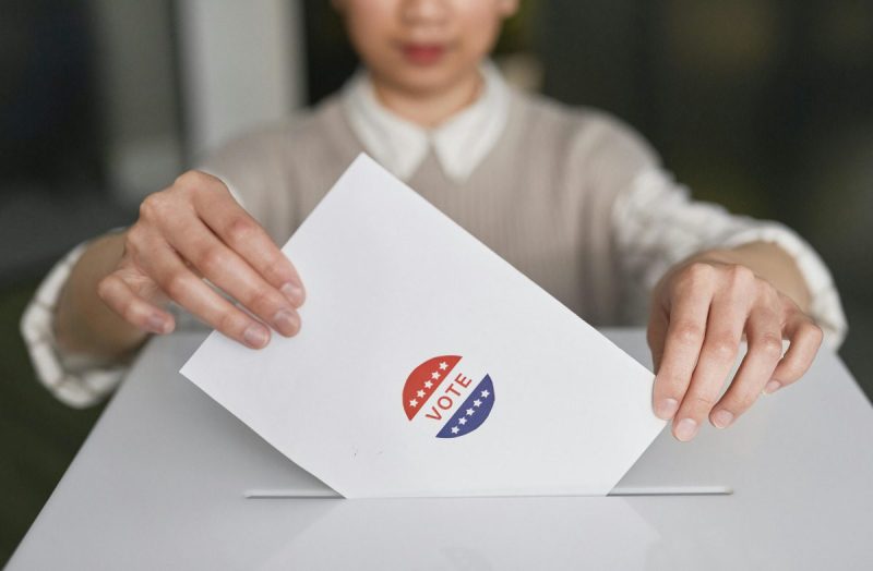 Woman holding an envelope with a Vote sticker on it.