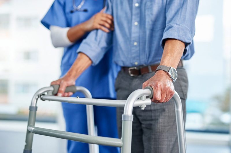 Shot of an unrecognizable female nurse helping a senior man walk using his walking frame at a nursing home. (Via Getty Images)