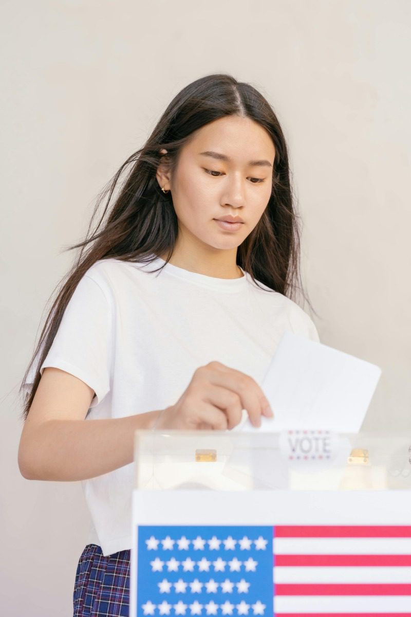 Young Asian woman casting her ballot to vote in an American flag box.
