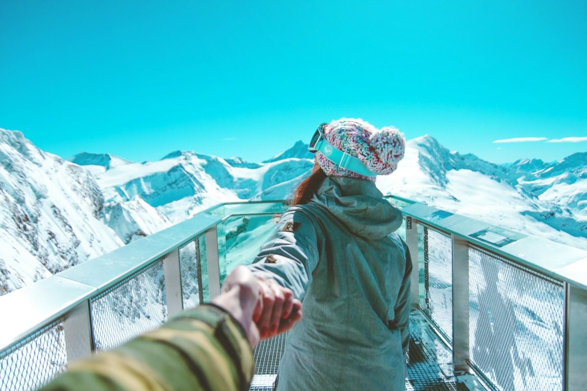 Couple holding hands looking over snowy mountains.