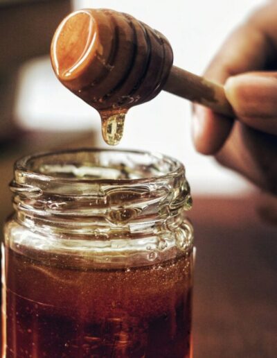 a hand holds a honey dipper outside of a jar of honey