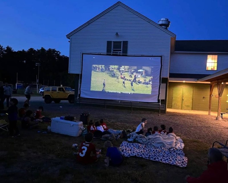 People watch a soccer game on a project screen set up in a residential yard